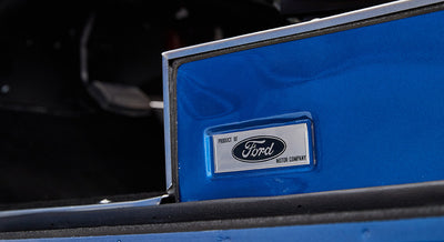 Silver badge reading 'Product of Ford Motor Company' on blue vehicle interior edge