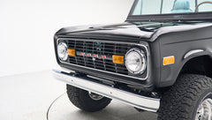 Classic Ford Bronco front corner showing grille, headlights, and chrome bumper in black paint