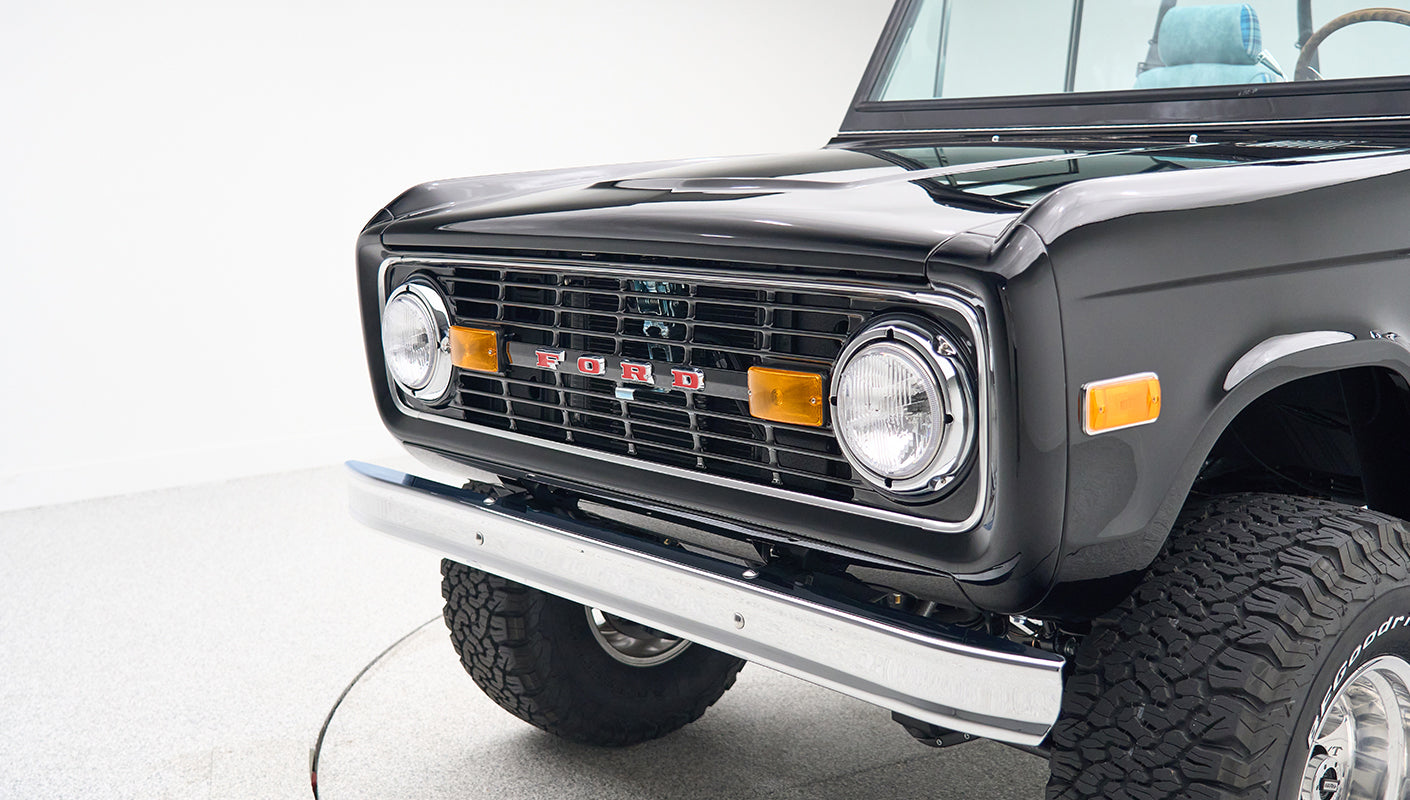 Classic Ford Bronco front corner showing grille, headlights, and chrome bumper in black paint