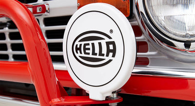 White HELLA branded round cover mounted on front of red vehicle grille near headlight