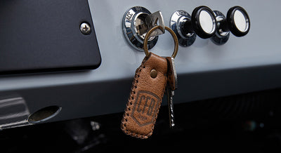 Brown leather keychain with embossed CFB Series logo hanging on car ignition with metal key inserted