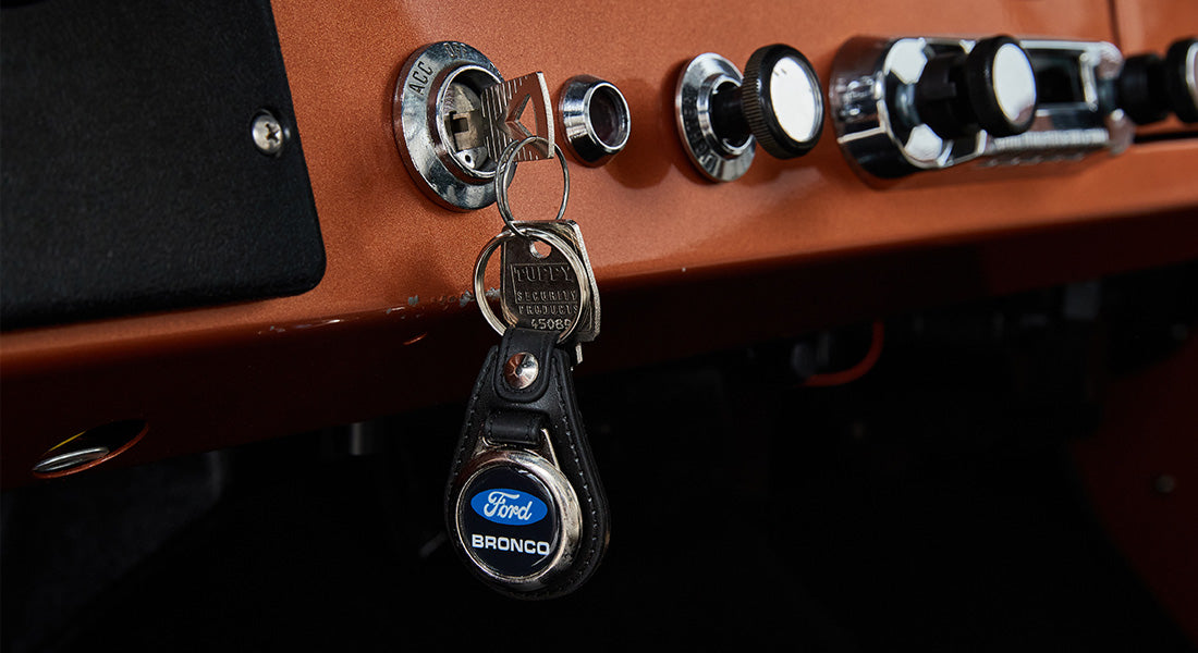 Key in ignition with Ford Bronco keychain hanging from orange dashboard with metal knobs