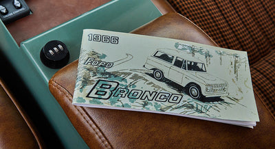 1966 Ford Bronco owner's manual booklet resting on brown leather seat armrest