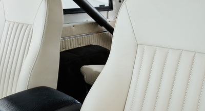 Close-up of white leather seats with stitch detailing and black armrest inside Classic Ford Bronco