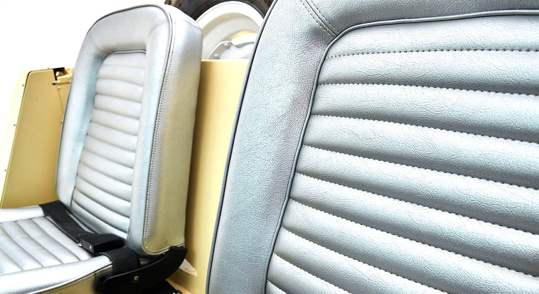 Close-up of two light gray vintage car seats with stitched horizontal panels, part of a Classic Ford Bronco.