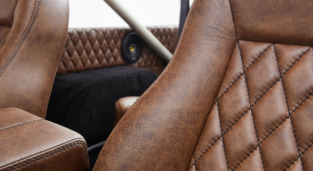 Brown leather seat with black stitching and visible part of classic vehicle interior