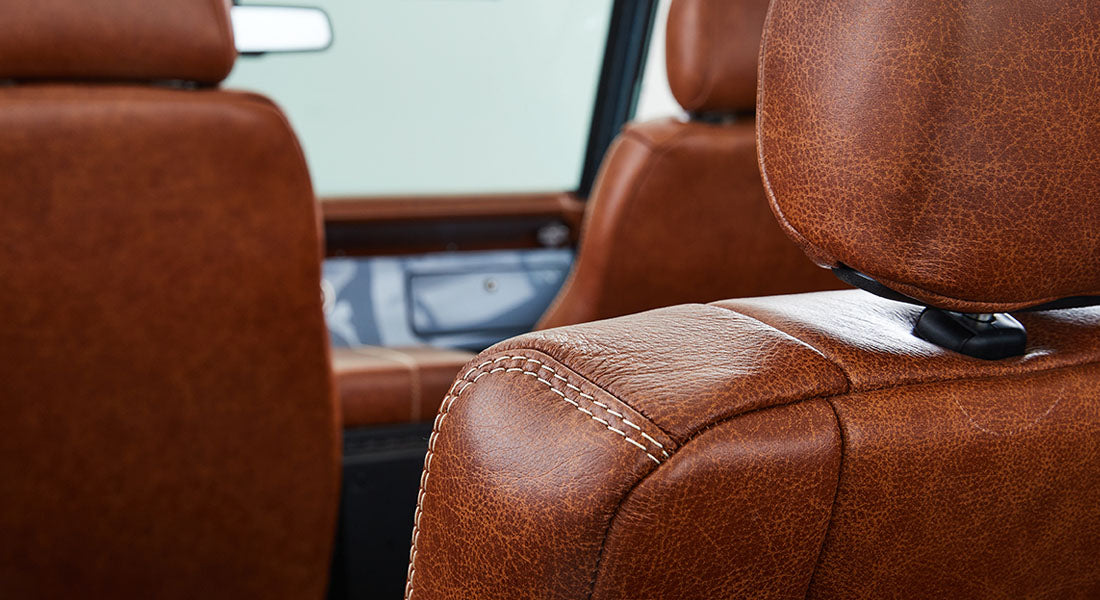 Brown leather car seats with visible stitching inside vehicle cabin with light-colored window background