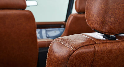 Brown leather car seats with visible stitching inside vehicle cabin with light-colored window background