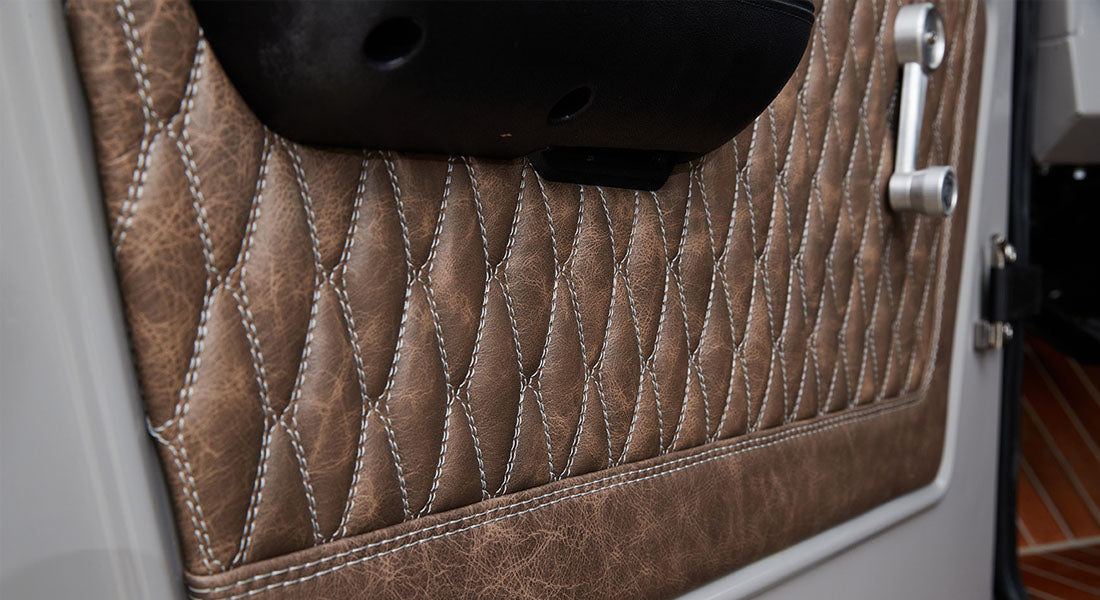 Close-up of brown textured quilted upholstery with white stitching on vehicle door interior