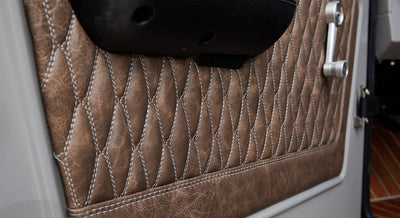 Close-up of brown textured quilted upholstery with white stitching on vehicle door interior