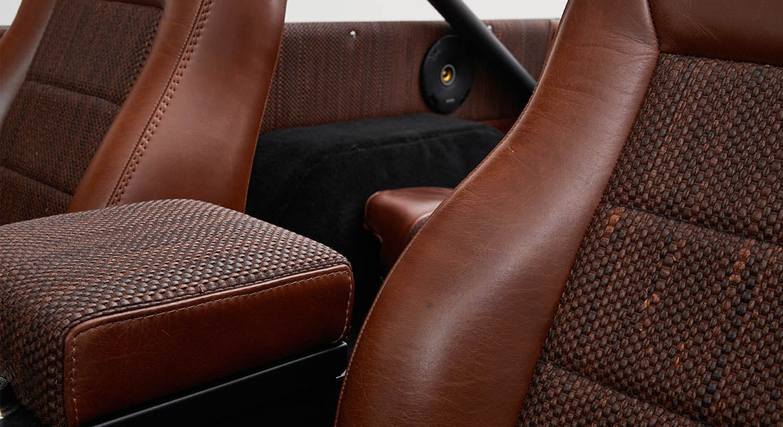 Two brown leather and woven fabric seats with black speaker in background inside Classic Ford Bronco