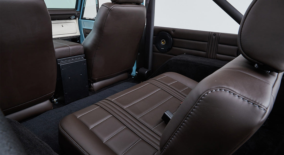 Interior rear seating area showing dark brown leather seats and speakers inside Classic Ford Bronco.