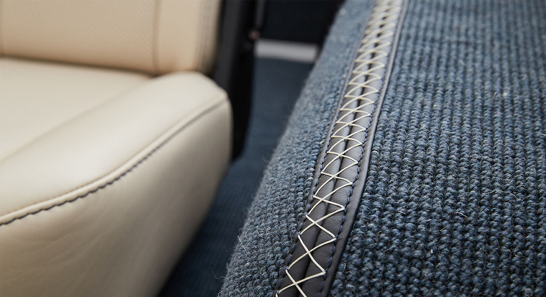 Side view of beige leather seat and dark woven carpet with detailed contrast stitching