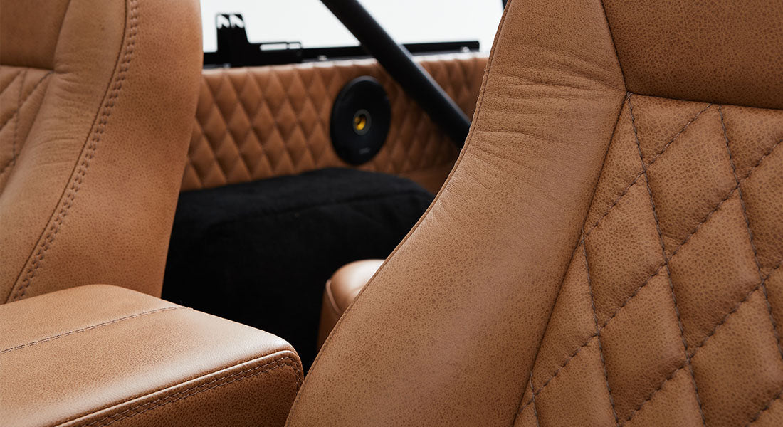 Tan leather seats and armrest inside a Classic Ford Bronco with diamond stitching and black carpet.