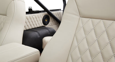 Two white leather seats with diamond stitching, part of vehicle interior with visible speaker and roll bar