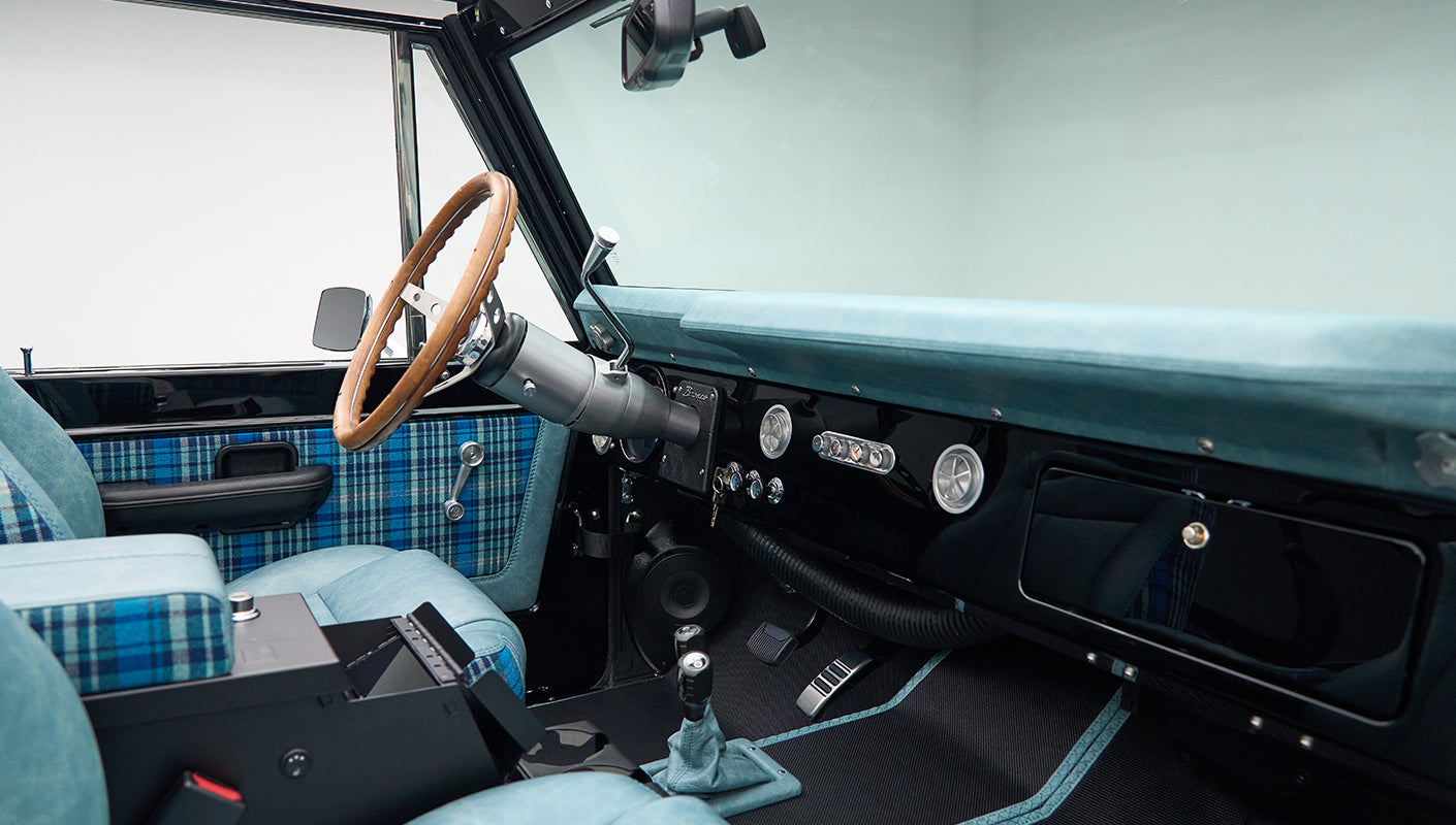 Classic Ford Bronco interior showing blue plaid upholstery on seats and door panel, brown steering wheel