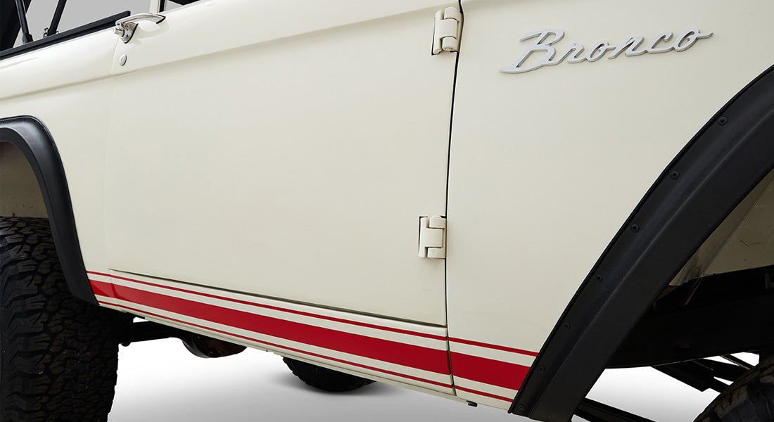 Side view of white Classic Ford Bronco with red stripes near bottom and Bronco emblem