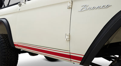 Side view of white Classic Ford Bronco with red stripes near bottom and Bronco emblem