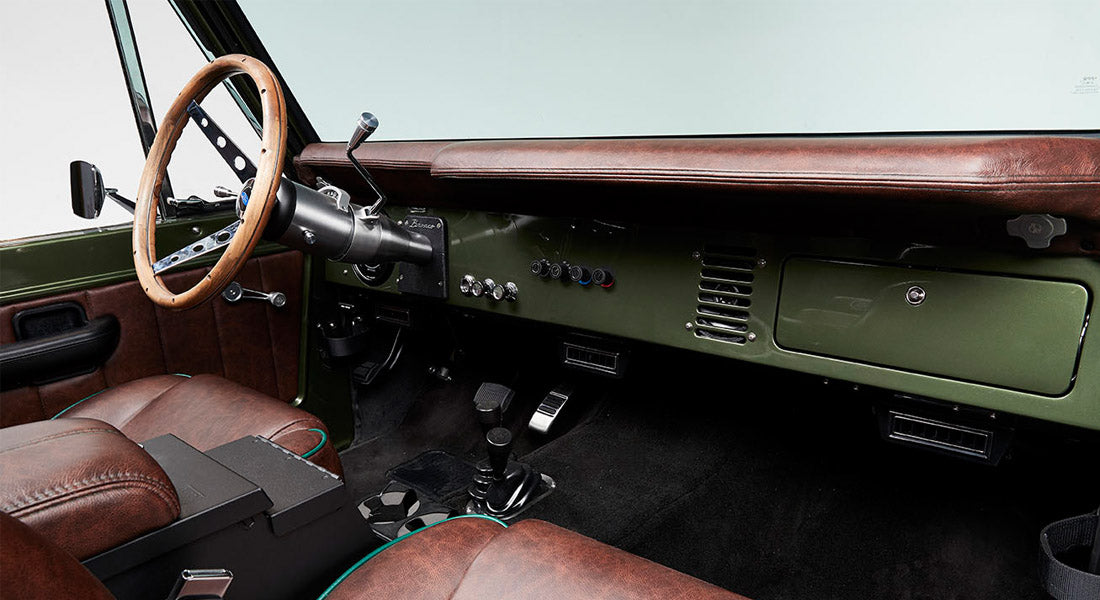 Classic Ford Bronco interior with brown leather seats, wooden steering wheel, and green dashboard