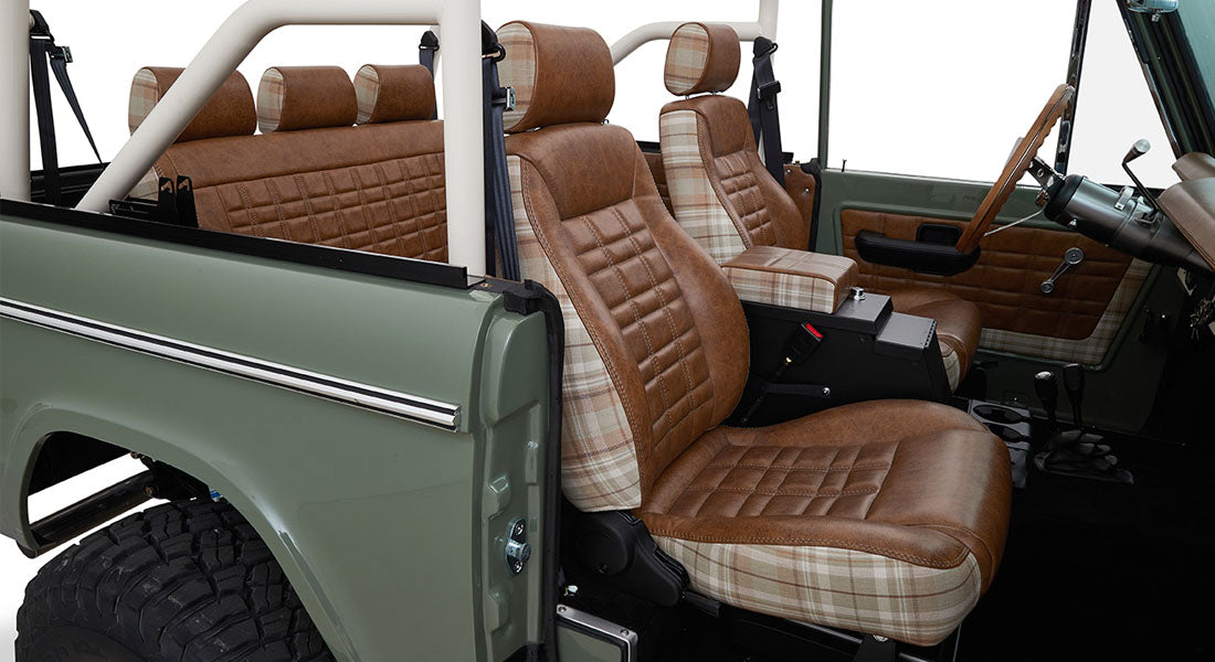 Interior passenger view showing brown and plaid seats with white roll cage inside a Classic Ford Bronco