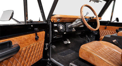 Classic Ford Bronco interior showing brown leather steering wheel, dashboard, pedals, and quilted brown panels
