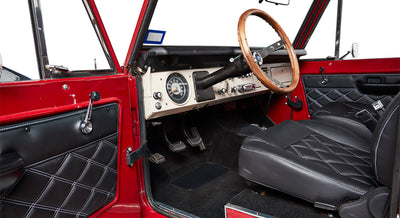 Interior of Classic Ford Bronco showing black quilted door panel, pedals, and red painted door frame.