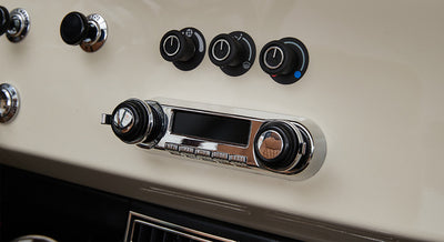 Chrome and black Retrosound audio controls and knobs on a cream dashboard of a Classic Ford Bronco
