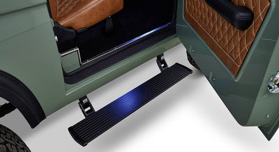 Black running board attached to open door of green Classic Ford Bronco with brown interior