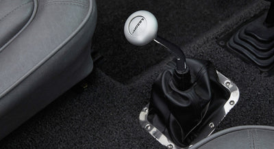 White round shift knob with custom logo on metal stick, mounted on black leather boot in Classic Ford Bronco interior