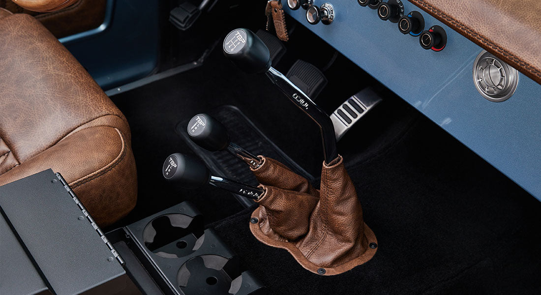 Three black manual shifters with leather boots inside the cabin of a Classic Ford Bronco