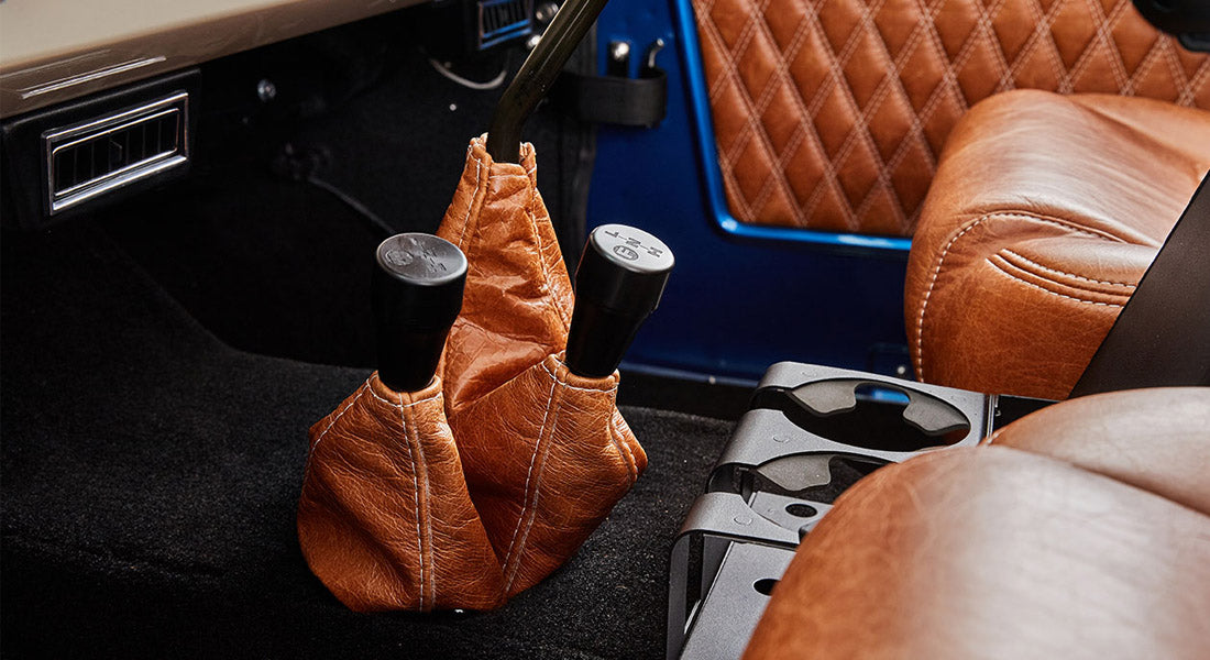 Two black shift knobs with leather boots between brown leather seats in Classic Ford Bronco interior.