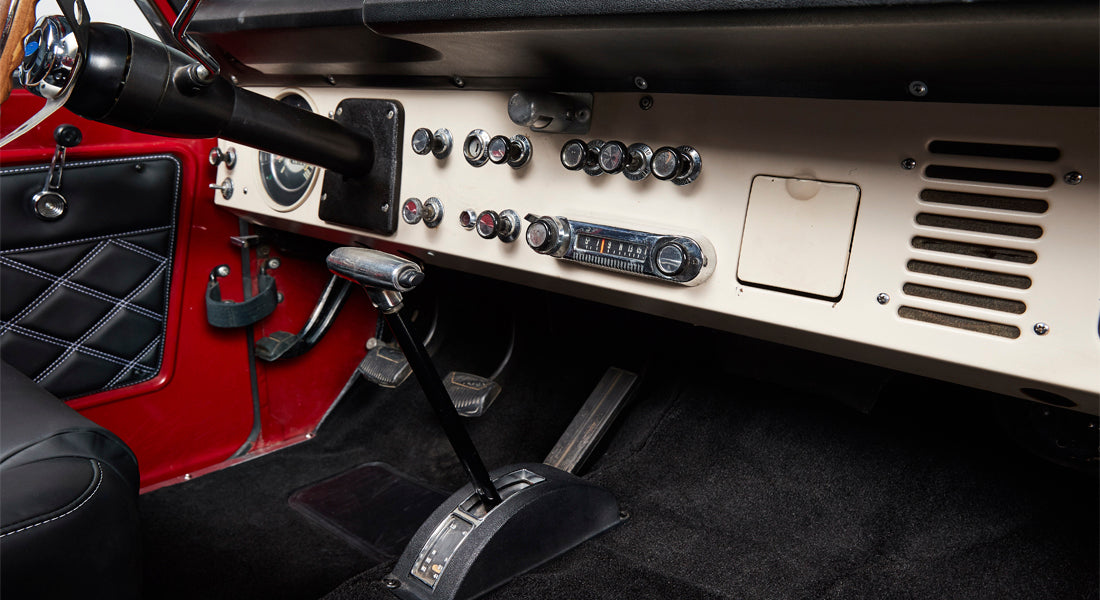 Classic Ford Bronco interior focused on dashboard and floor-mounted gear shifter with black seats.