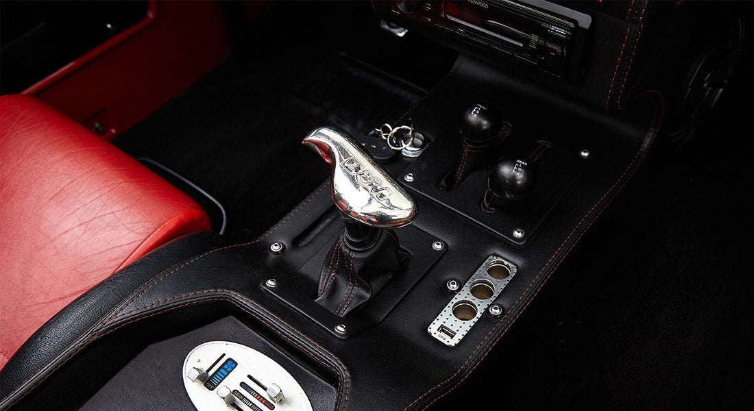 Black center console with a chrome Ford-branded gear shifter and two black control knobs on a Classic Ford Bronco