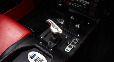 Black center console with a chrome Ford-branded gear shifter and two black control knobs on a Classic Ford Bronco