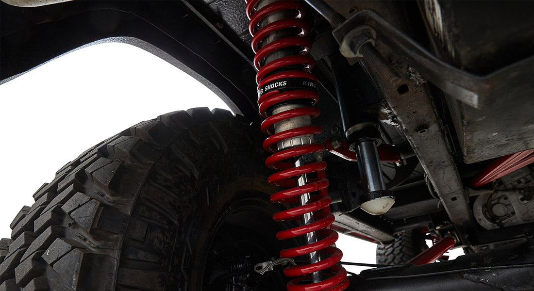 Red coil spring and black shock absorber above rugged off-road tire under vehicle frame