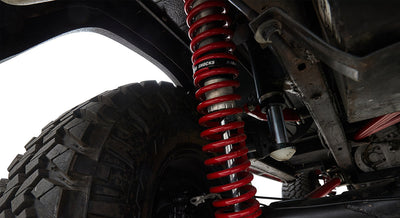 Red coil spring and black shock absorber above rugged off-road tire under vehicle frame