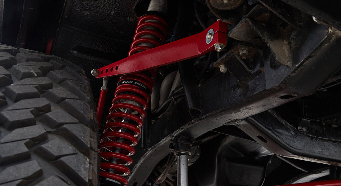 Red suspension components, coil spring and control arm, attached to chassis above large off-road tire