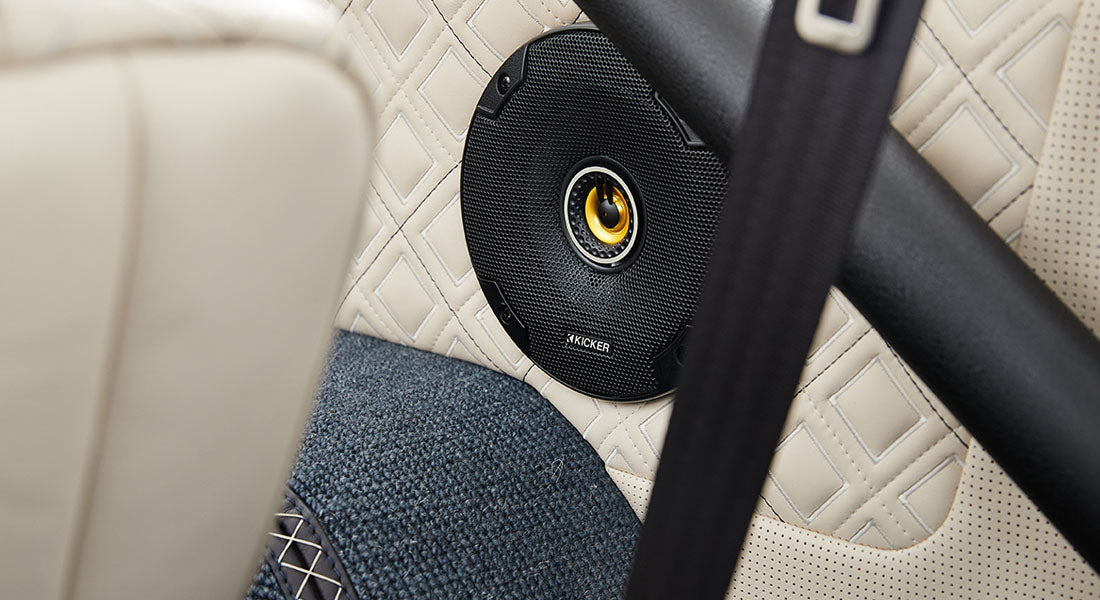 Close-up of round black speaker mounted on quilted beige door panel with blue carpet