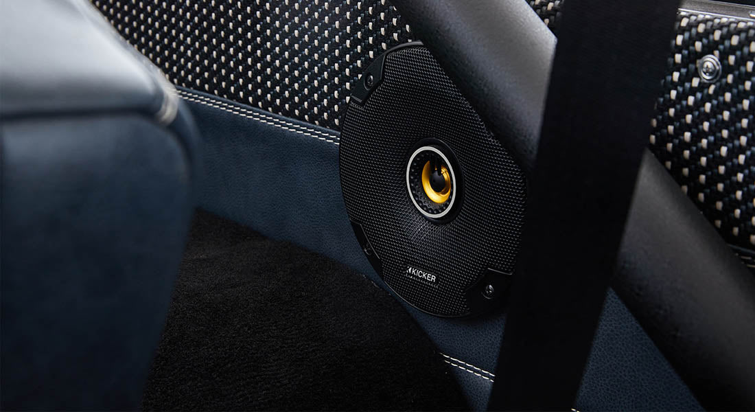 Black circular Kicker speaker mounted on dark blue car door panel with leather and fabric trim