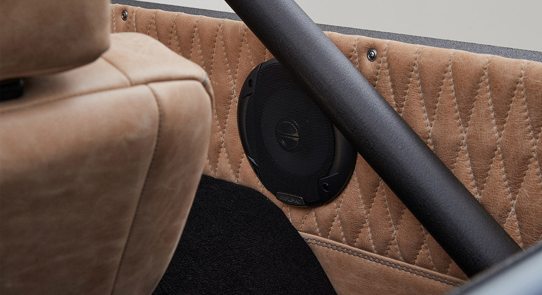 Speaker mounted on quilted tan leather interior panel with a seat and black roll bar nearby