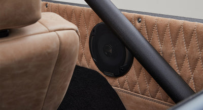 Speaker mounted on quilted tan leather interior panel with a seat and black roll bar nearby