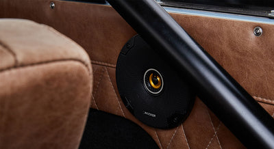 Black circular Kicker speaker installed in tan quilted leather interior panel with black roll cage