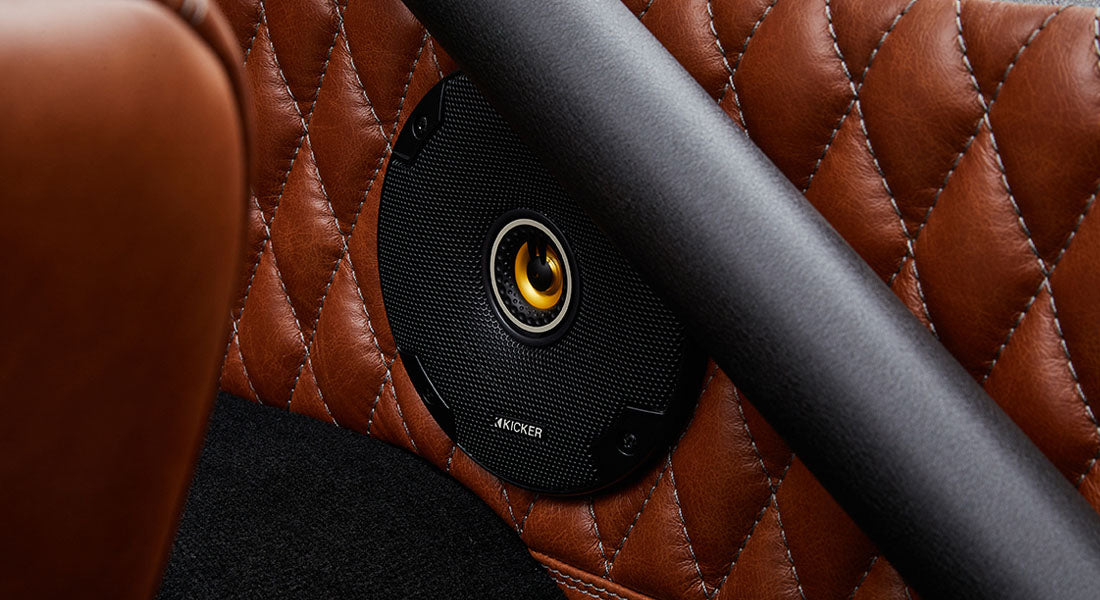Close-up of round black speaker mounted on brown quilted leather panel inside a Classic Ford Bronco