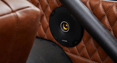 Black round speaker mounted on quilted brown leather door panel of Classic Ford Bronco