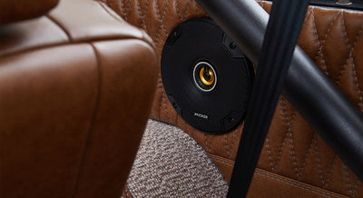 Round speaker mounted in quilted brown leather interior panel near a brown leather seat