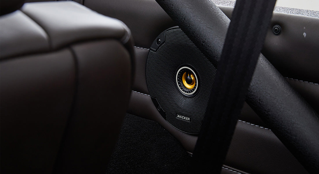 Black Kicker speaker mounted in door panel with leather upholstery and roll cage structure inside Classic Ford Bronco.