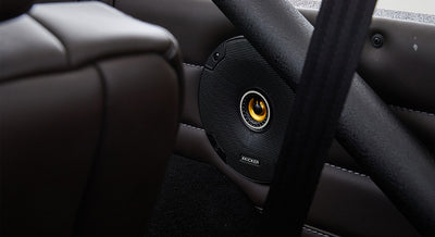 Black Kicker speaker mounted in door panel with leather upholstery and roll cage structure inside Classic Ford Bronco.