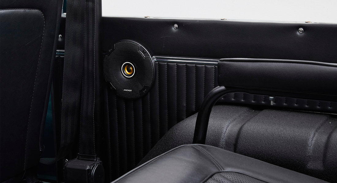 Close-up of a black speaker mounted on the interior side panel near a seatbelt and a black seat