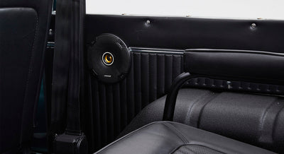 Close-up of a black speaker mounted on the interior side panel near a seatbelt and a black seat