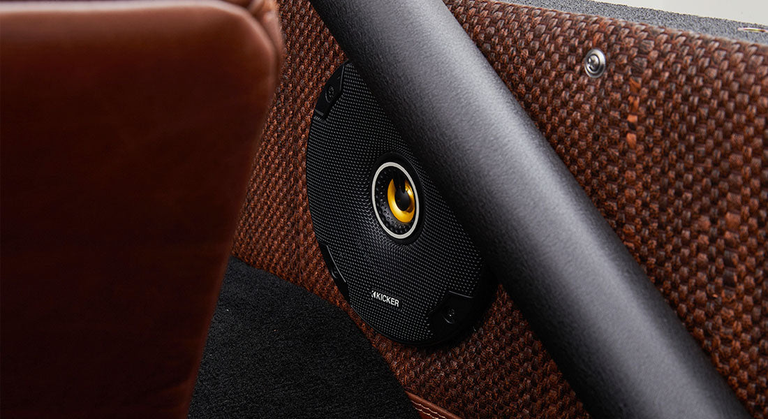 Black round speaker with yellow center mounted on brown patterned interior panel
